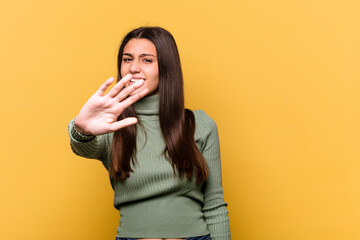 Young Indian woman isolated on yellow background rejecting someone showing a gesture of disgust.