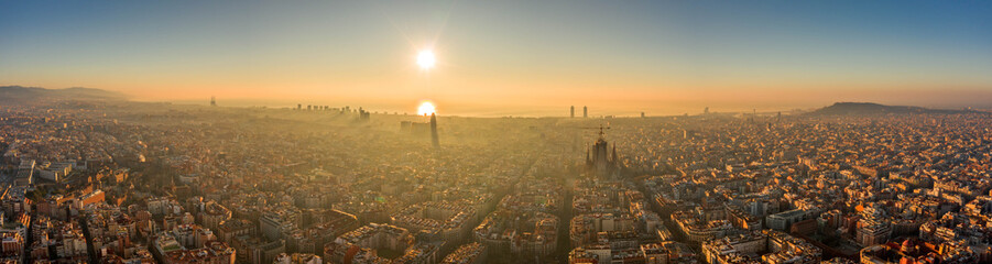 Aerial panorama drone shot of skyline in Barcelona center in misty morning foggy sunrise golden glow in Spain winter
