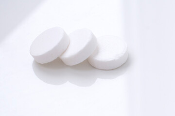 Fototapeta na wymiar Macro shot of three white tablets on white background with shadows. Antacids pills for relief stomachache from excess gastric acid in stomach. Stress induce gastric ulcer treatment concept.