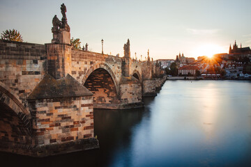 famous stone bridge in Prague in the Czech Republic known as Charles Bridge connects parts of the city across the Vltava River at sunset. Long exposure of river, sun and Charles Bridge