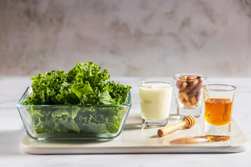 Kale in a glass bowl with greek yogurt, almond ann honey in glass on white table background for healthy smoothie. Kale is considered a superfood because it's a great source of vitamins and minerals.