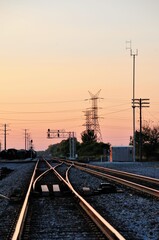 Fototapeta na wymiar Mainline railroad tracks disappearing into the horizon at dusk as they pass under a series of power lines near Elgin, Illinois. The tracks connect with Chicago, about 40 miles to the southeast.