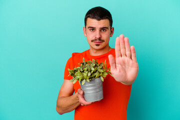 Young caucasian man holding a leaf isolated on blue background standing with outstretched hand showing stop sign, preventing you.