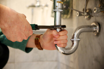 Plumber fixing sink pipe with adjustable wrench.