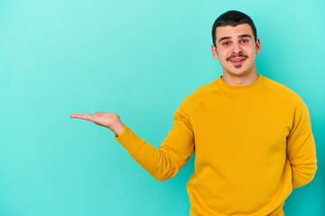 Young caucasian man isolated on blue background showing a copy space on a palm and holding another...