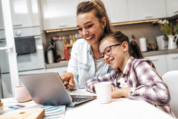 Happy mother with her young daughter enjoying in online shopping or working from home. Business from distance and virtual communication with family and friends.
