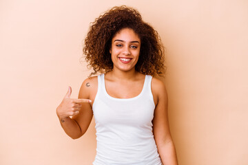 Young african american woman isolated on beige background person pointing by hand to a shirt copy space, proud and confident