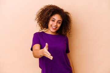Young african american woman isolated on beige background stretching hand at camera in greeting gesture.