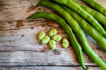 Group of raw tender beans, next to some green pods, on a wooden background.