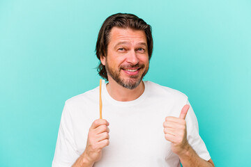 Middle age dutch man holding a toothbrush isolated on blue background smiling and raising thumb up