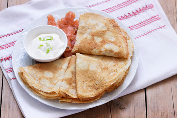 Thin pancakes with salmon and sour cream on a light background. Rustic style.