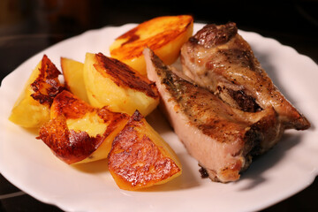 Baked meat with potatoes on a white plate. Appetizing crispy crust on food.