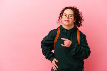 Young student woman with Down syndrome isolated on pink background smiling and pointing aside,...