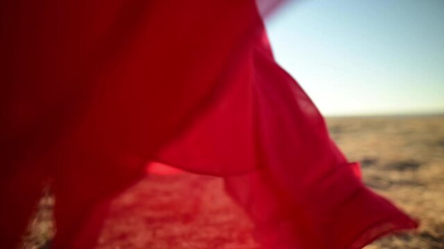 close-up female Slender legs in sandals in a red loose transparent dress that flutters in the wind in waves goes on dry grass in nature. Low angle slow motion. Backlight with glare