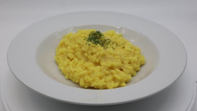 Italian Risotto allo Zafferano (rice with saffron) in a white dish on rotating display.