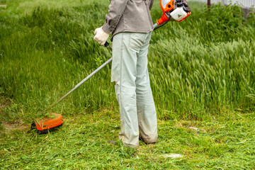 A man in work clothes mows tall grass with a trimmer in the garden