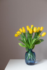 bouquet of yellow tulips in blue glass vase on table. Cozy home concept. vertical image.