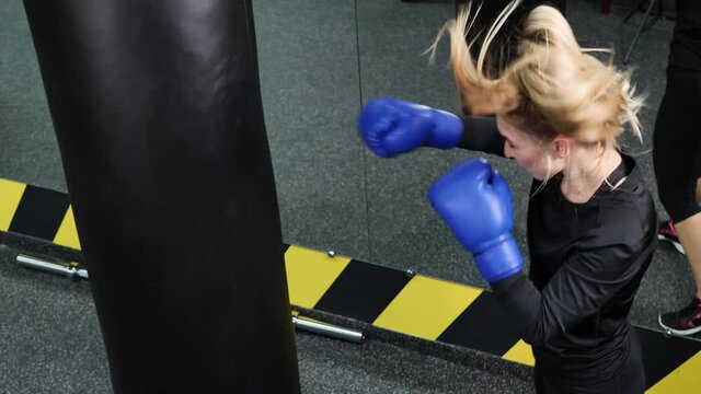 Young female athlete in blue boxing gloves hits a pear in the ring.