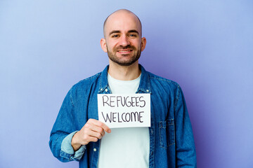 Young caucasian bald man holding a Refugees welcome placard isolated on blue background happy,...