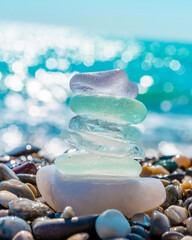 Sea glass stones arranged in a balance pyramid on the beach. Beautiful azure color sea with blurred...