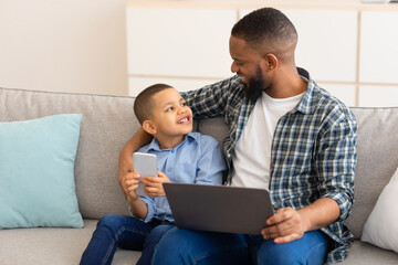 African Father And Son Using Laptop And Phone At Home