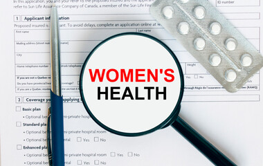 Magnifying glass with text Women's Health inside lies on medical documents with pills and a blue metal pen