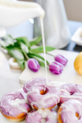 Fototapeta na wymiar Homemade Purple donuts on dessert stand with Spring flowers