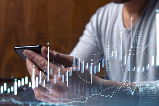 Trader holding in the hands a smart phone and researching stock market to proceed right investment solutions. Internet trading and wealth management concept. Hologram Forex chart over close up shot.