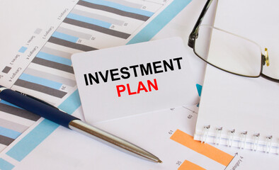 Business card with text Investment Plan lies on financial charts with pen and eyeglass