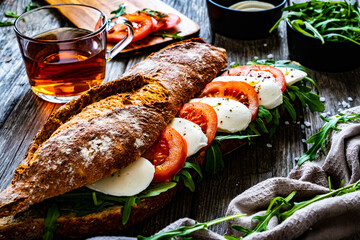 Caprese sandwich with tomato, mozzarella and arugula on wooden table