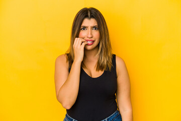 Young indian woman isolated on yellow background biting fingernails, nervous and very anxious.