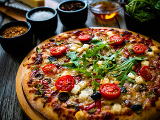 Pizza with goat cheese, tomatoes, olives, parmesan and mozzarella on wooden table
