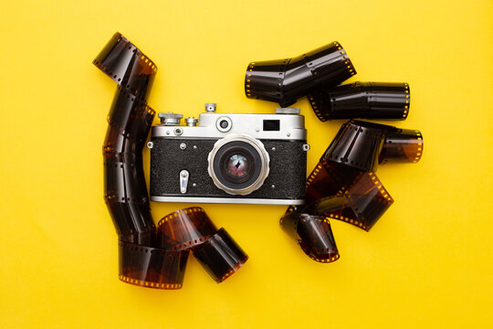retro camera belted with photographic film on a yellow background flat lay