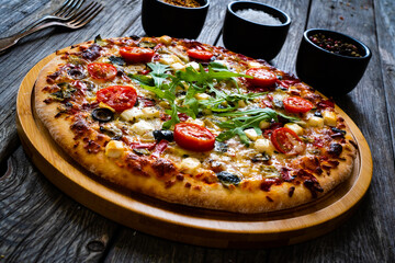 Pizza with goat cheese, tomatoes, olives, parmesan and mozzarella on wooden table
