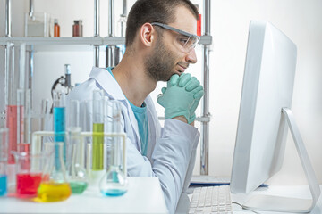 Chemistry laboratory assistant in protective glasses smiling looks in computer display.
