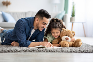 Loving arabic dad reading book to his cute little daughter at home