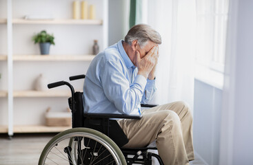 Unhappy and lonely senior handicapped man in wheelchair crying at home