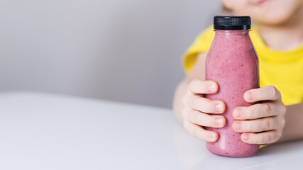 Berry smoothie in a plastic bottle in the hands of a child. Copy space.