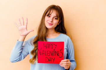 Fototapeta na wymiar Young caucasian woman holding a Happy Valentines day isolated smiling cheerful showing number five with fingers.