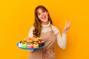 Young pastry chef woman isolated on yellow background joyful and carefree showing a peace symbol with fingers.