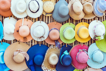 A variety of fashionable and colorful hats hanging on the bamboo backdrop of curbside shop.Women's designer hats from the sun of different colors. Design of women's beach hats. Beach hats for summer.