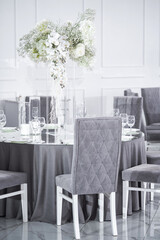 Festive dining table in gray with a floral arrangement of white phalinopsis flowers. Wedding banquet.