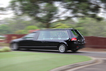A generic black hearse with a coffin driving through a cemetery. Motion blur - obrazy, fototapety, plakaty