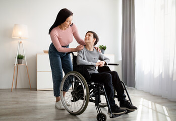 Full length portrait of mother and her disabled son in wheelchair looking at each other and smiling...