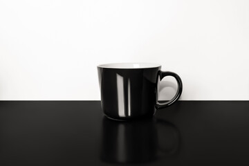 Black mug. On a black background near a light wall.