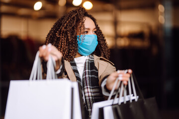 Obraz premium Portrait of beautiful african american woman in protective medical mask after shopping near the store. Shopping during the coronavirus Covid-19 pandemic. Sales And Discount, Retail, Purchase.