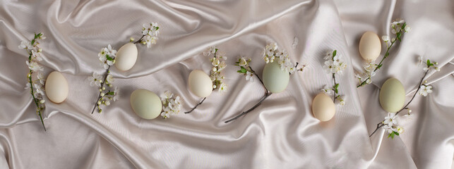 Wide Easter. backgrouond with eggs and spring blossoms on a silky satin fabric