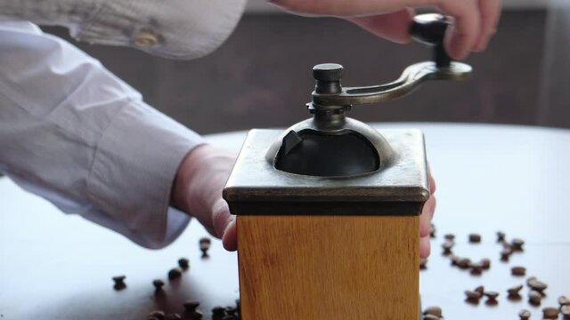 Man grinds coffee beans in a manual vintage coffee grinder, close-up