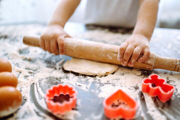 Little child  roll out the dough with a rolling pin on a wooden surface, close-up.  Small hands preparing dough for baking. Easter baking preparation. Cookies for Christmas.