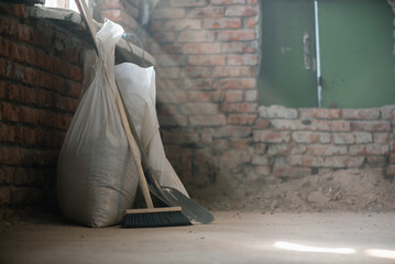 Shovel, broom and bags with a construction garbage on the dusty construction site floor background.